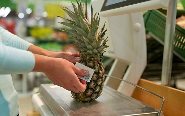 woman weighing pineapple on scale at grocery store